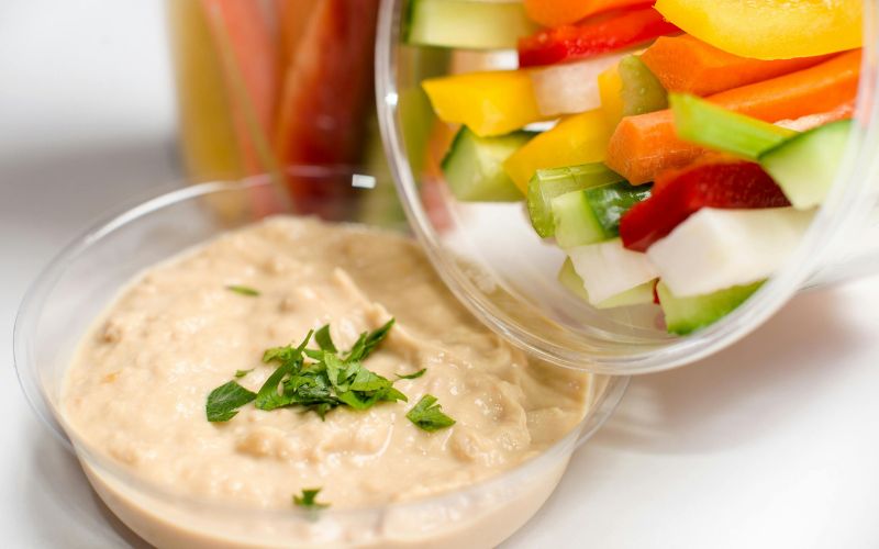 Homemade beer cheese dip in a clear bowl with fresh herbs and sliced peppers and cucumbers. 
