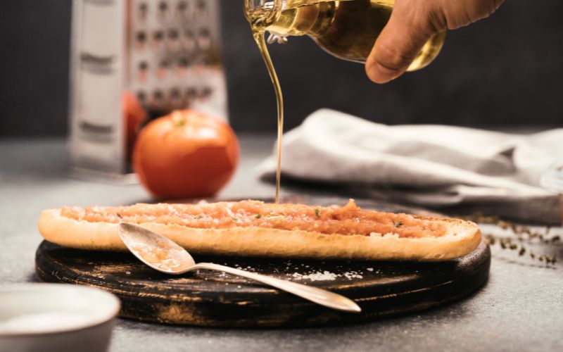 Pouring olive oil over bread and grated tomatoes