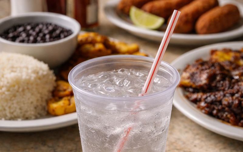 Water in a cup surrounded by cuban black beans, white rice, croquettes.