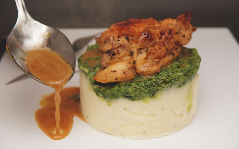 Pan sauce being poured over potatoes and chicken